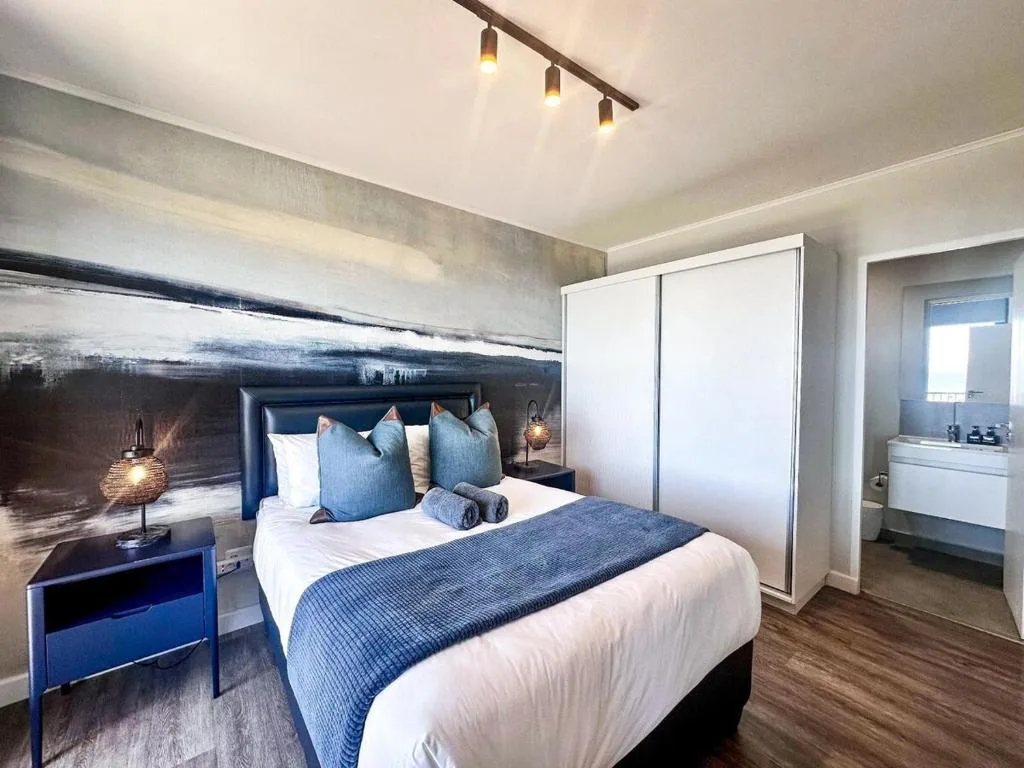 Modern bedroom with queen bed, blue accent pillows, contemporary artwork above headboard