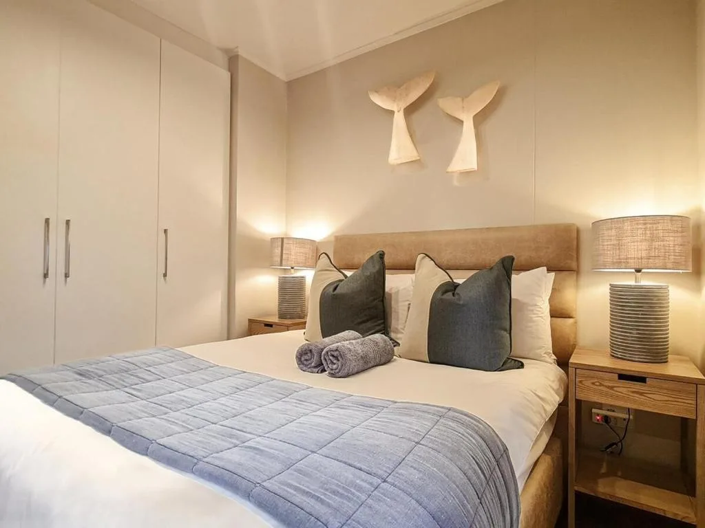 Modern bedroom with queen bed, neutral bedding, whale tail wall art, and warm lighting
