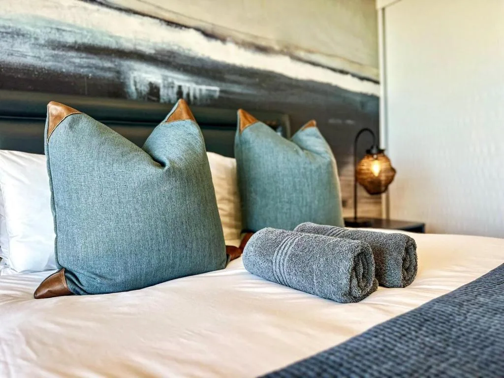 Bed with teal pillows, rolled towels, and decorative lamp fixture