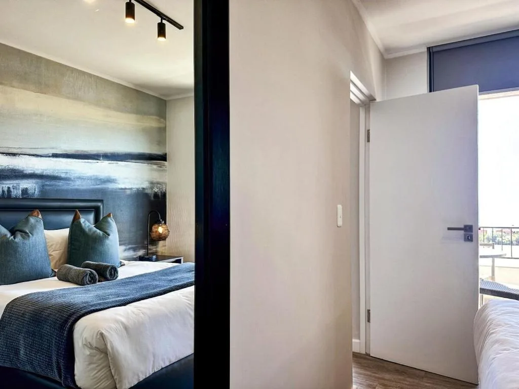 Modern bedroom with white bedding, blue accent pillows, and contemporary wall art