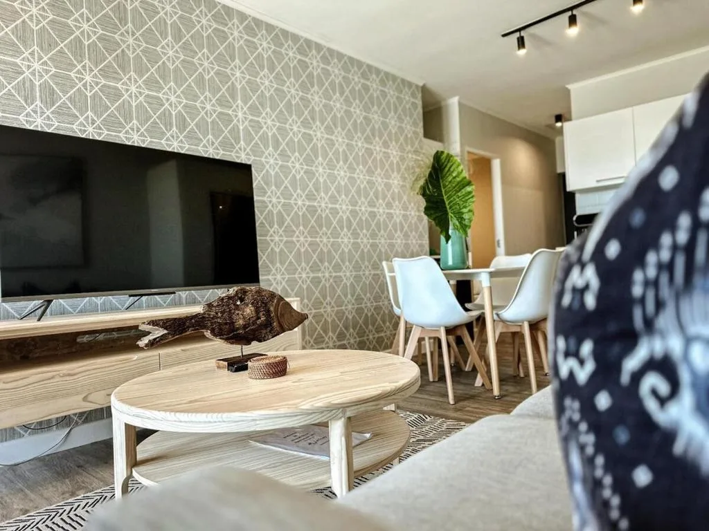 Modern lounge with wooden coffee table, TV, and dining area beyond
