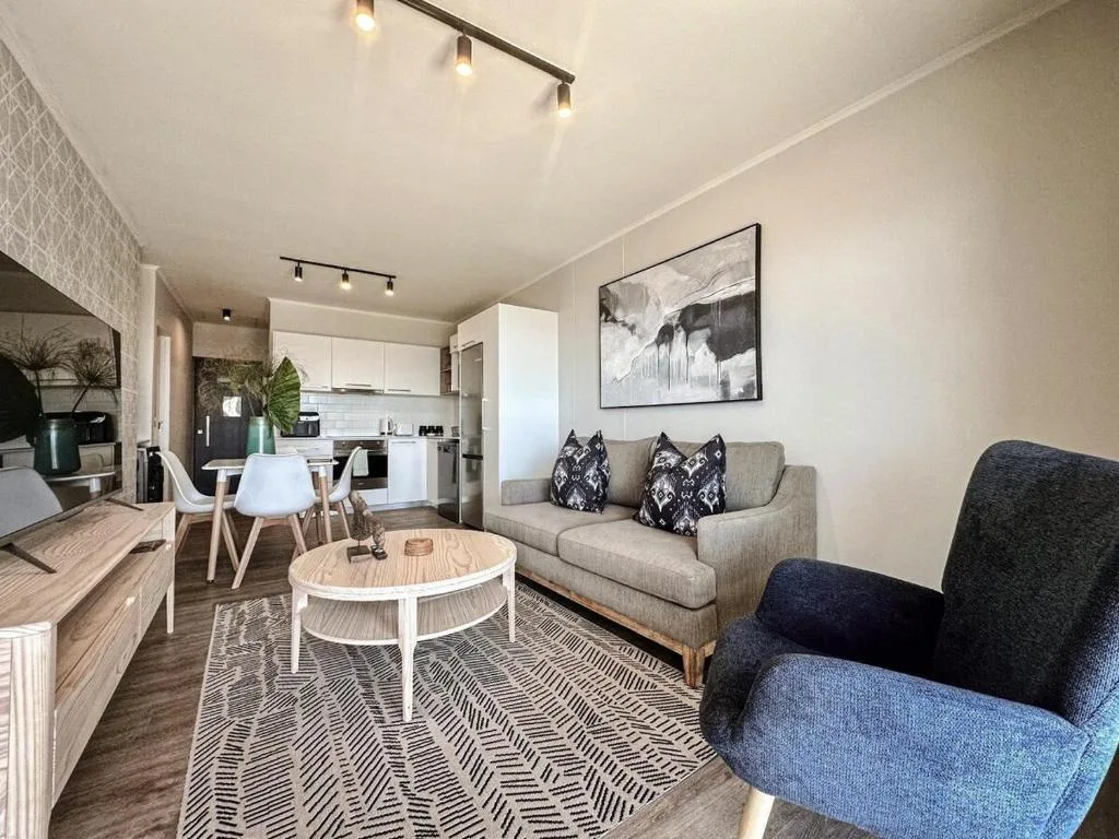 Modern lounge with gray sofa, armchair, and open-plan kitchen area