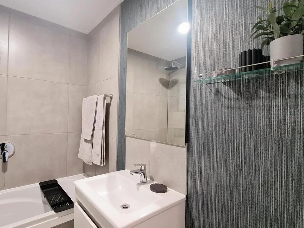 Modern bathroom with white sink, mirror, shower enclosure and tiled walls