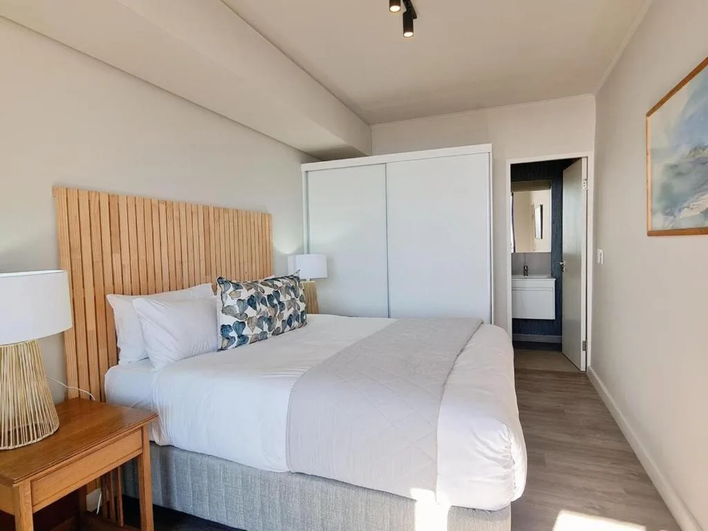 Modern bedroom with queen bed, wooden headboard, and ensuite bathroom access