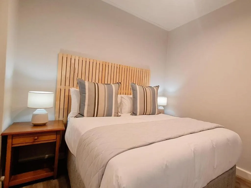 Bright bedroom with queen bed, striped pillows, wooden headboard, bedside table