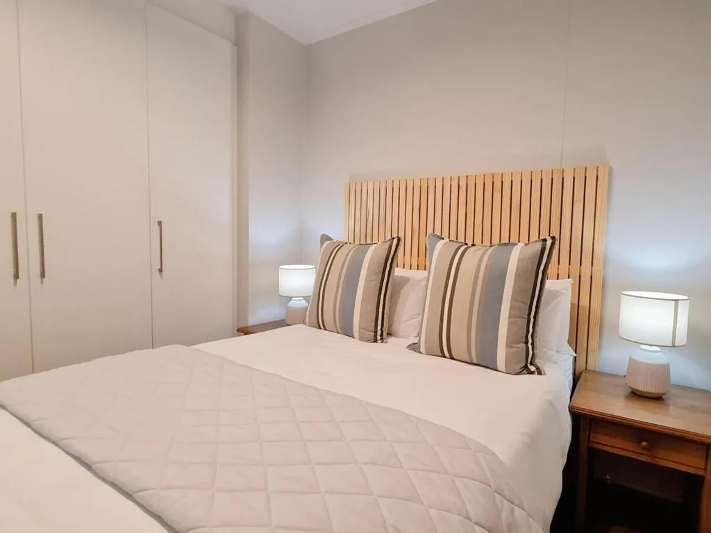 Modern bedroom with white bedding, striped pillows, wooden headboard, and built-in wardrobe