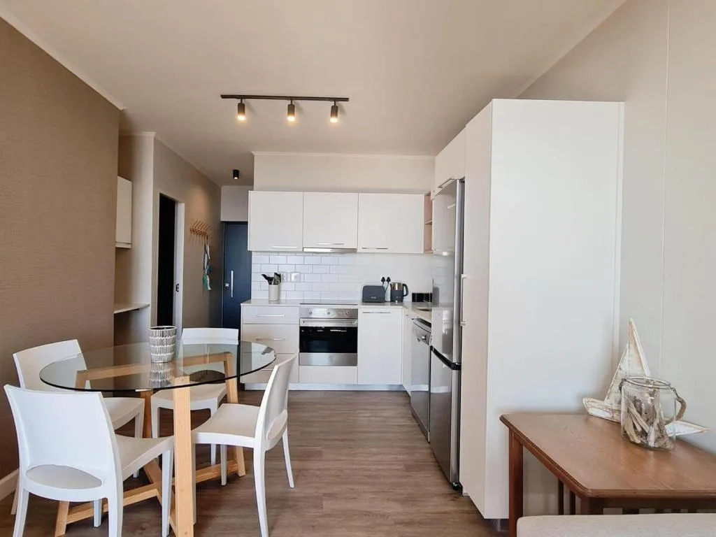 Modern white kitchen with dining area, stainless steel appliances, and pendant lighting