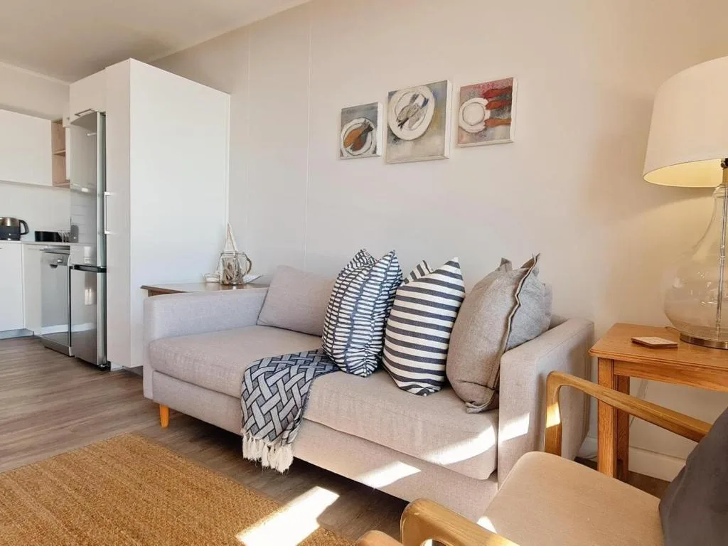 Light-filled living room with beige sofa, striped cushions, and kitchen glimpse