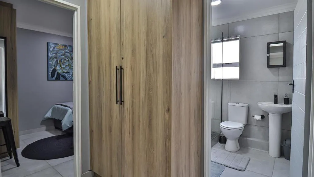 Modern bathroom with white tiles, toilet, sink vanity, and wood-grain shower enclosure