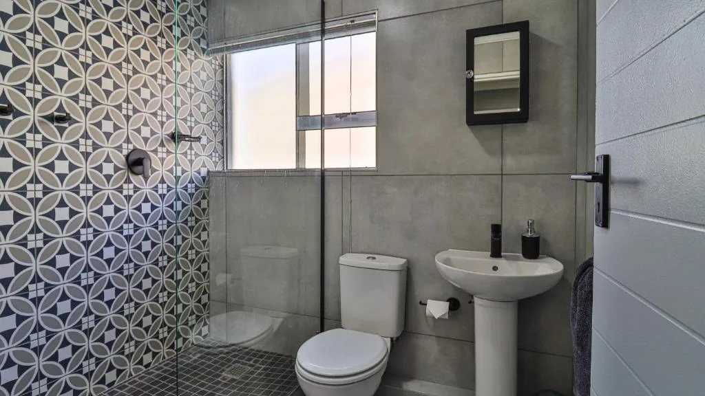 Modern bathroom with patterned tile shower, toilet, and pedestal sink