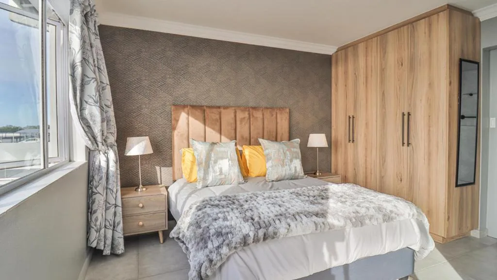 Modern bedroom with queen bed, wooden wardrobe, and ocean views through large windows