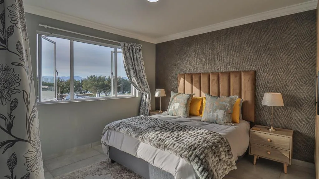Modern bedroom with ocean view, tan headboard, layered bedding, stylish lamps
