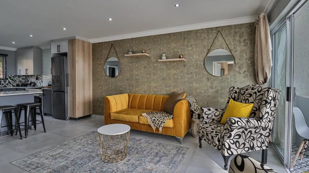Modern lounge with golden sofa, patterned armchair, and open-plan kitchen area