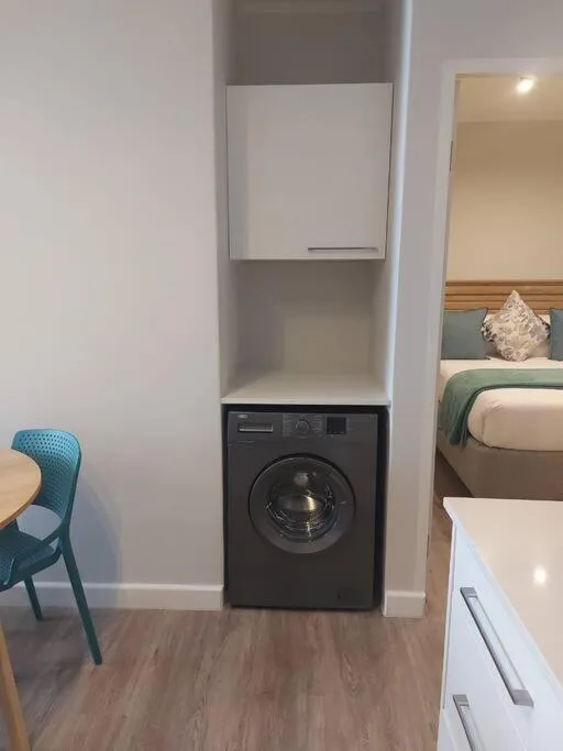 Built-in black washing machine in bedroom alcove with storage above