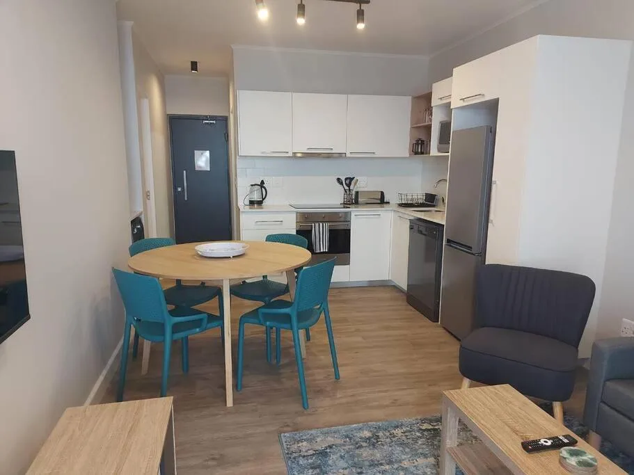 Modern open-plan kitchen with white cabinetry, round dining table, and teal chairs