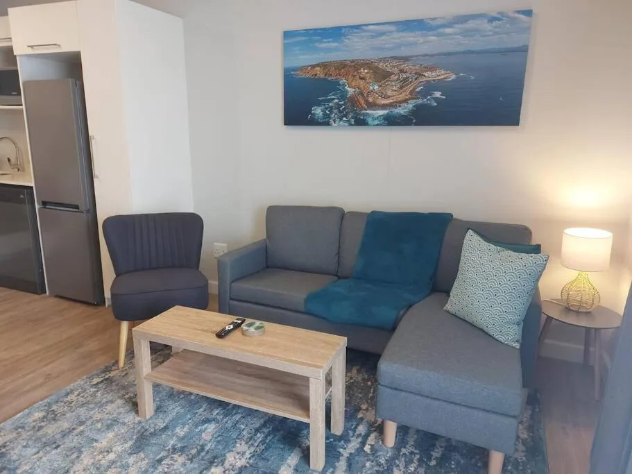 Modern lounge with gray sofa, accent chair, wooden coffee table, and coastal artwork