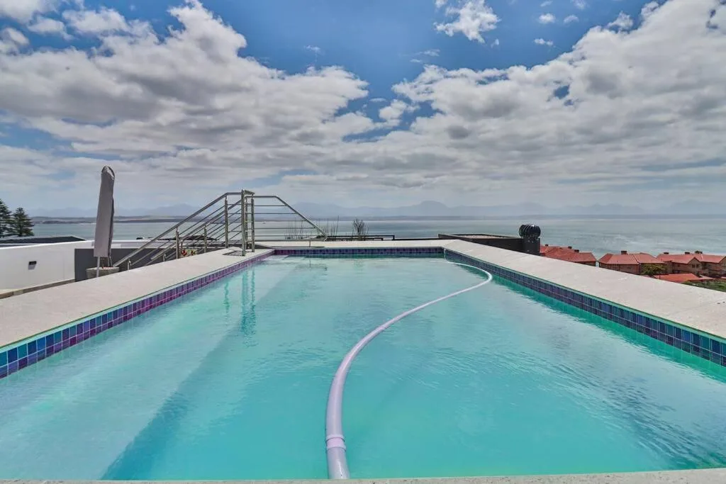 Turquoise swimming pool with ocean and mountains visible in background