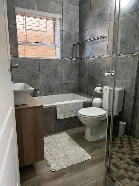 Modern bathroom with grey tile walls, white basin, toilet, and walk-in shower