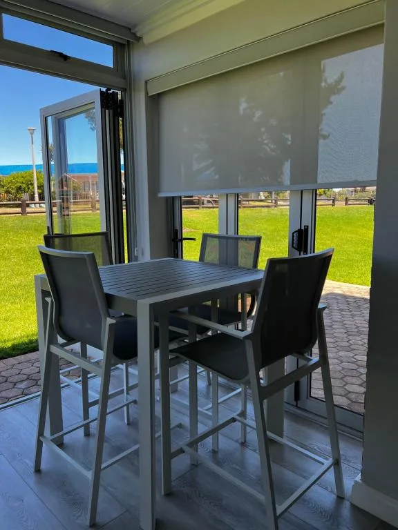 Outdoor dining area with high table and chairs overlooking ocean and green lawn