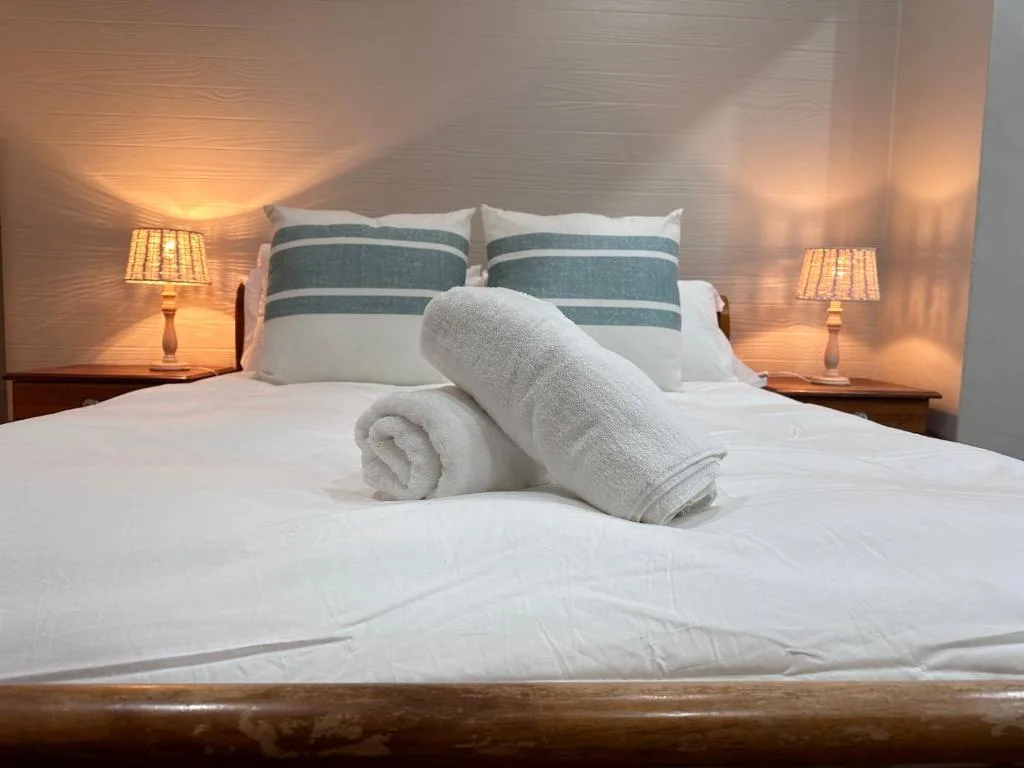 Bed with striped pillows, white linens, rolled towels, bedside lamps