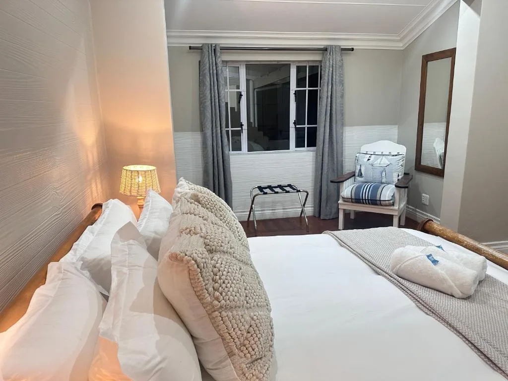 Bright bedroom with queen bed, cream cushions, bedside lamp, and glass doors opening to deck