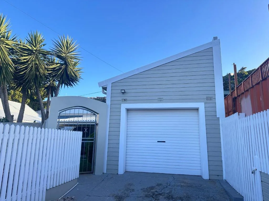 Modern gray and white villa with garage, white fencing, and palm trees