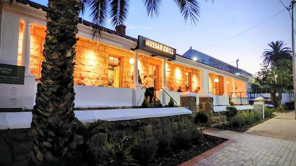 Illuminated white villa facade at dusk with palm trees and restaurant signage