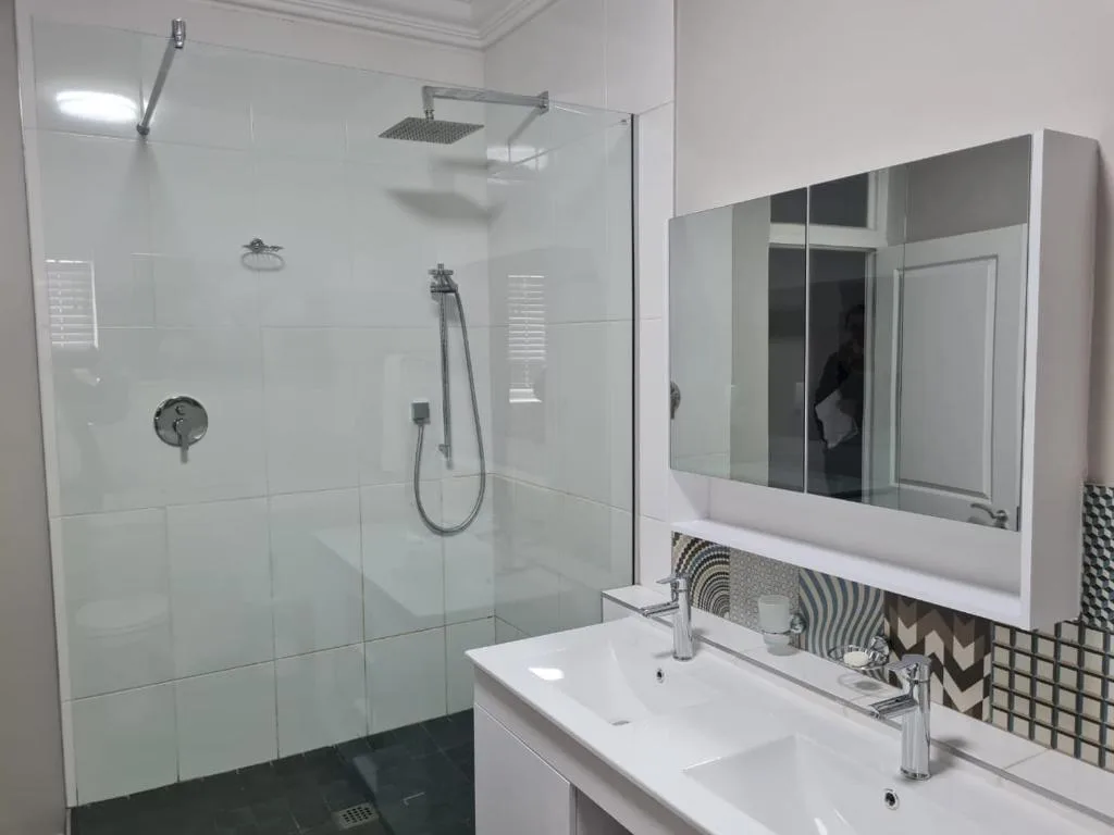 Modern bathroom with walk-in shower, dual vanity, and mirrored cabinet