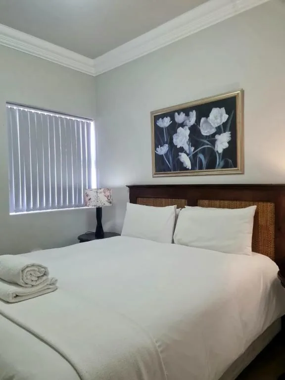 Bright bedroom with white bedding, wooden headboard, and floral artwork