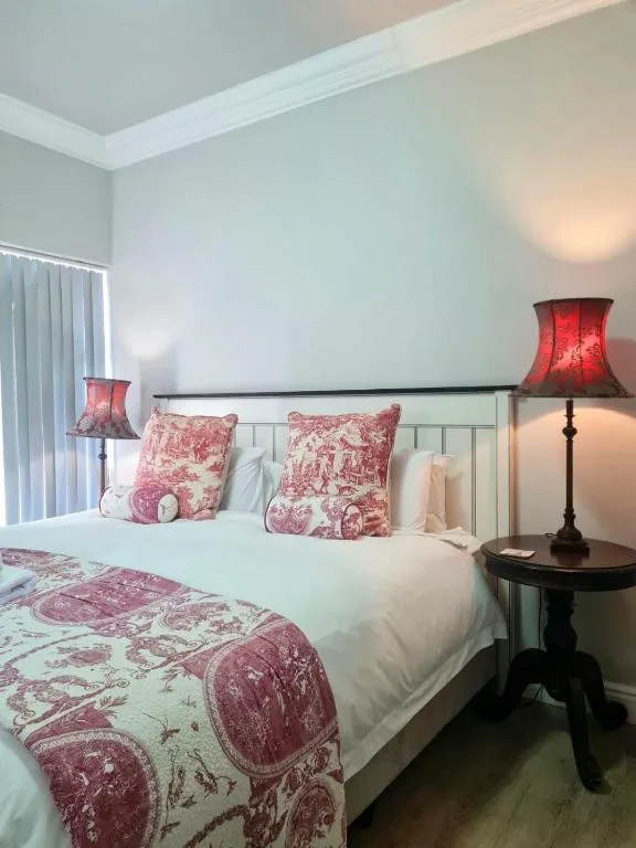 Bright bedroom with white bed, red patterned pillows and bedding, bedside lamps