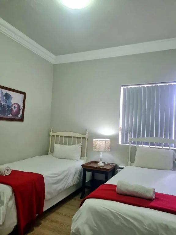 Twin bedroom with white beds and red blankets, beside lamp and window