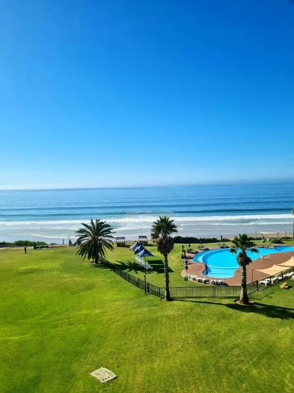 Oceanfront vista with pool, palm trees, and sandy beach below