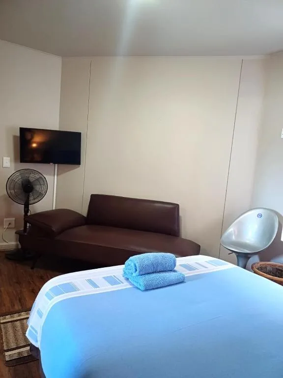 Bright bedroom with bed, lounge seating, wall-mounted TV, and fan