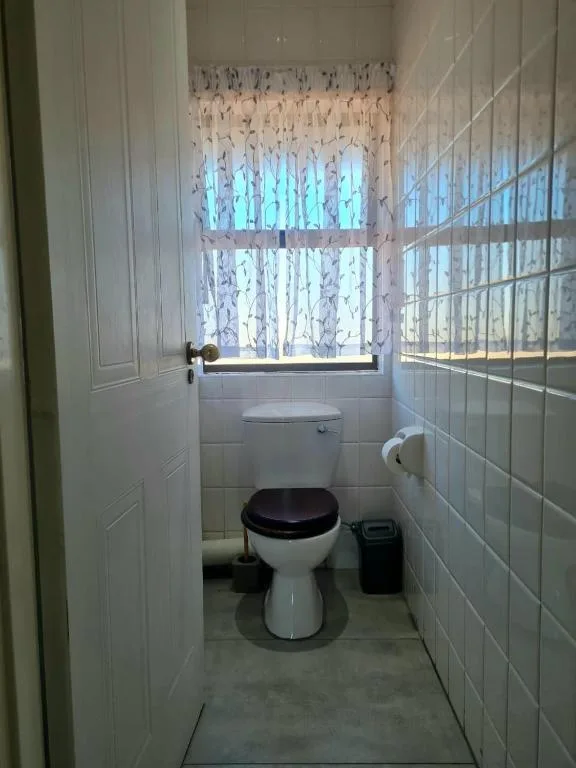 Compact bathroom with white toilet, tiled walls, and natural window light