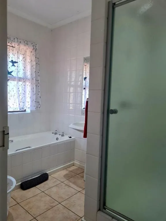 Clean bathroom with bathtub, tiled walls, window with curtains and shower enclosure