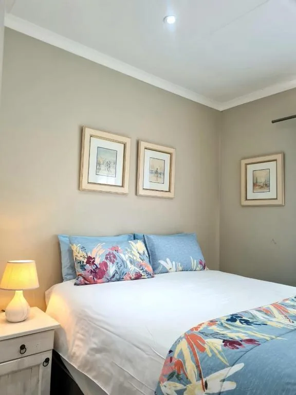 Bright bedroom with queen bed, blue pillows, floral bedding, and framed artwork