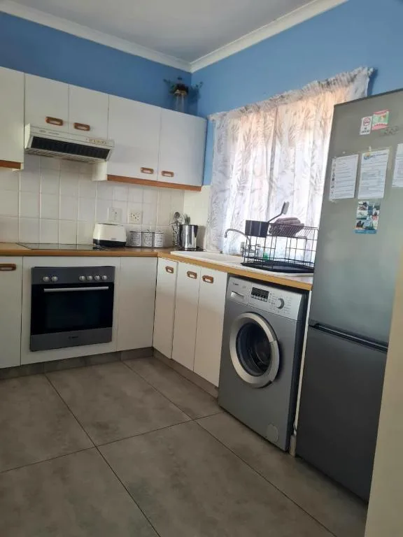 Compact kitchen with cream cabinetry, oven, washing machine, and refrigerator