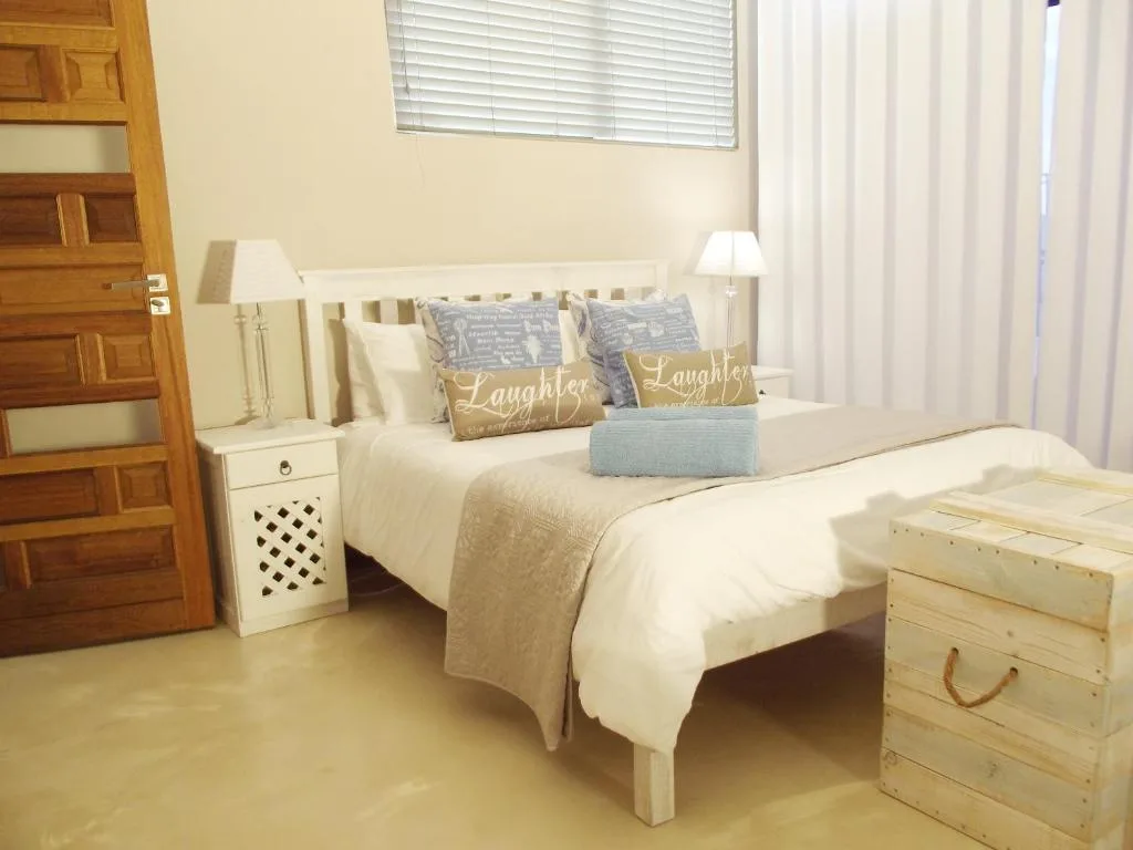 Bright bedroom with white bed, decorative pillows, wooden door, and side table