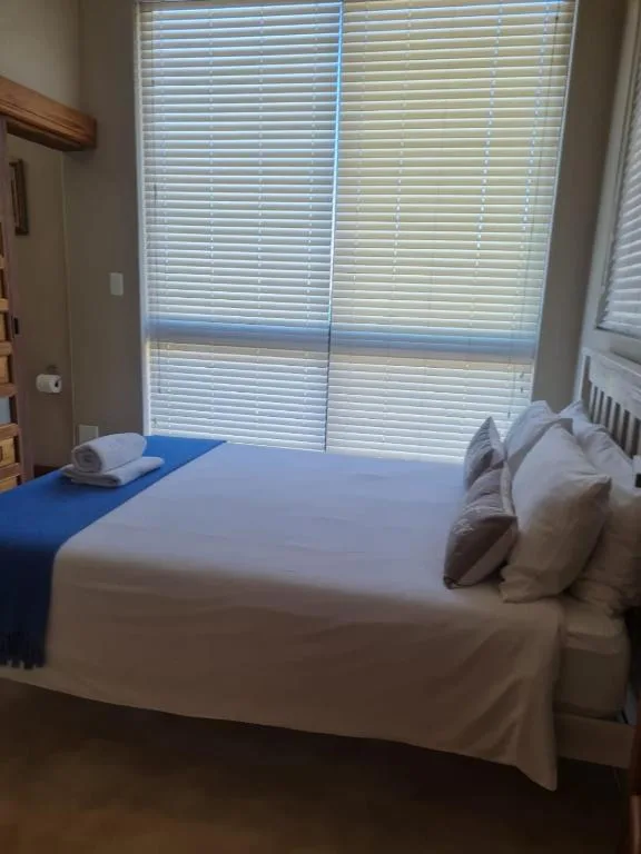Bright bedroom with white bedding, blue accent, and large shuttered windows