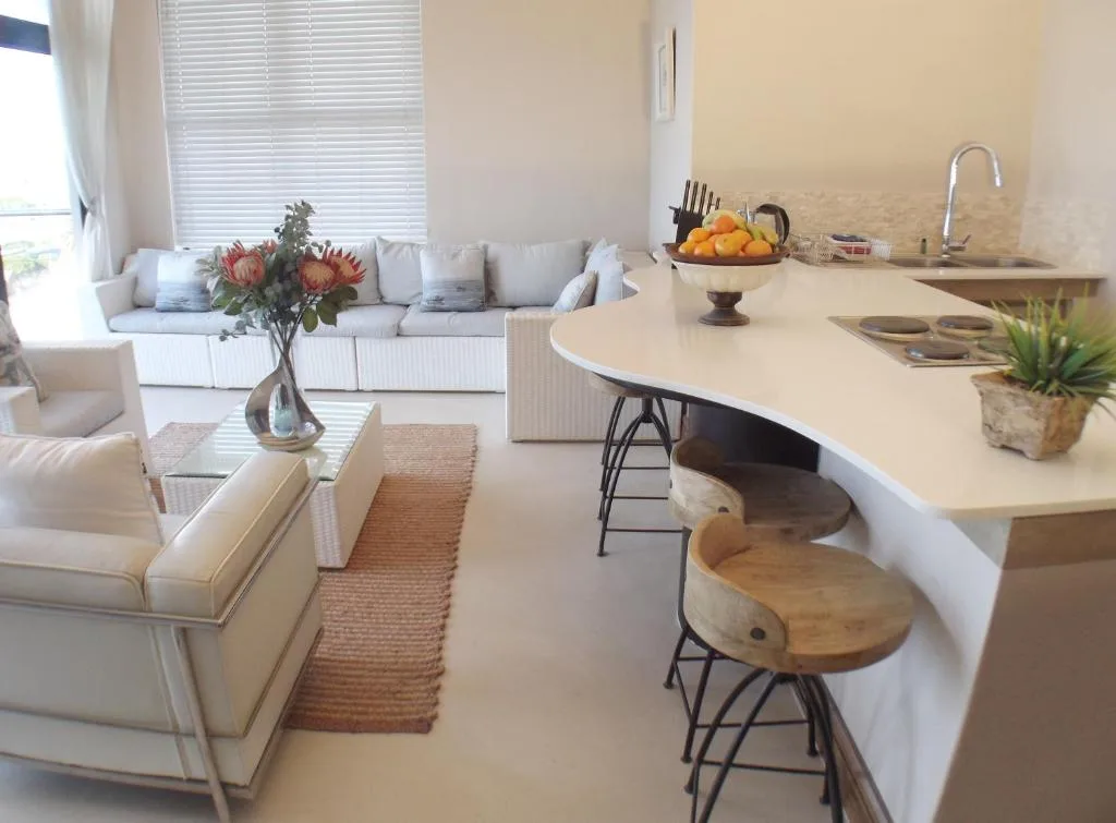 Open-plan lounge and kitchen with cream sofa, dining counter, and fresh flowers