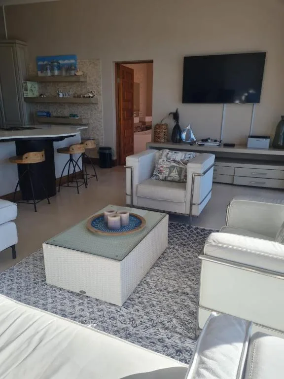 Modern lounge with cream armchairs, wall-mounted TV, and kitchen area visible