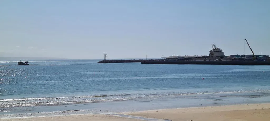 Pristine beach with turquoise water and industrial ships offshore