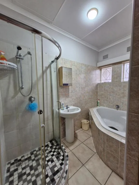Modern bathroom with shower enclosure, pedestal sink, and white bathtub