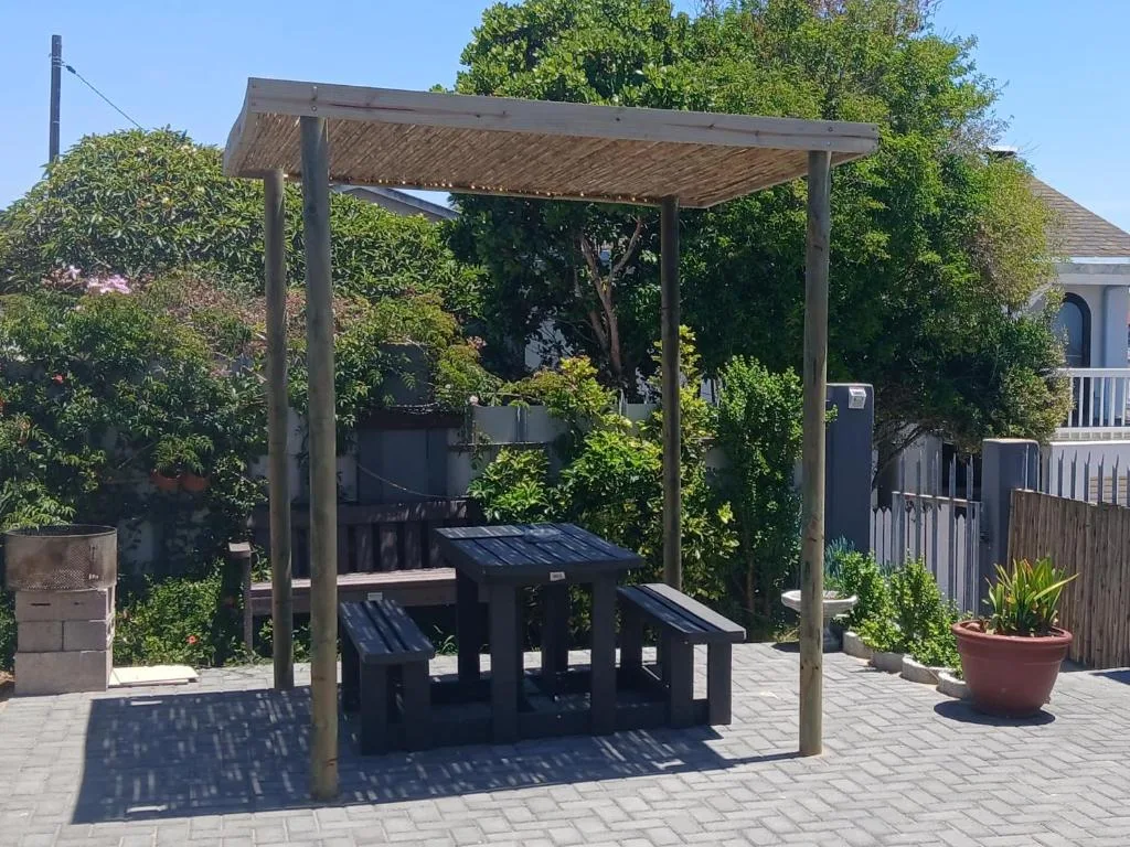 Shaded pergola with braai and outdoor seating area surrounded by lush gardens