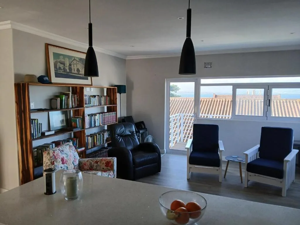 Modern lounge with black leather seating, wooden bookshelf, and ocean view