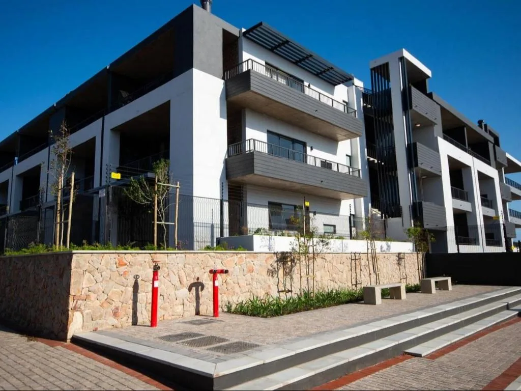 Modern multi-story apartment building with white and dark facade, balconies, and stone wall entrance