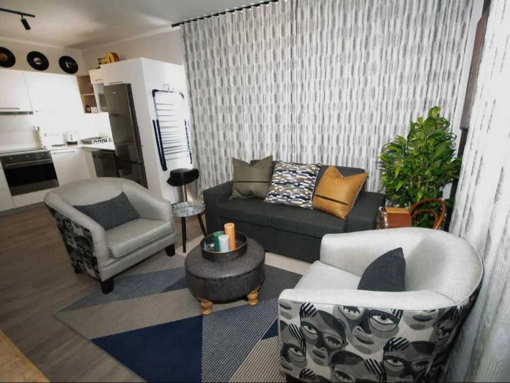Modern lounge with dark sofa, patterned armchairs, and open-plan kitchen visible