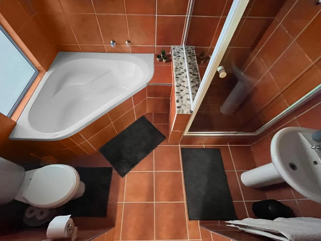 Overhead view of spacious bathroom with corner bath, toilet, sink, and terracotta tiles
