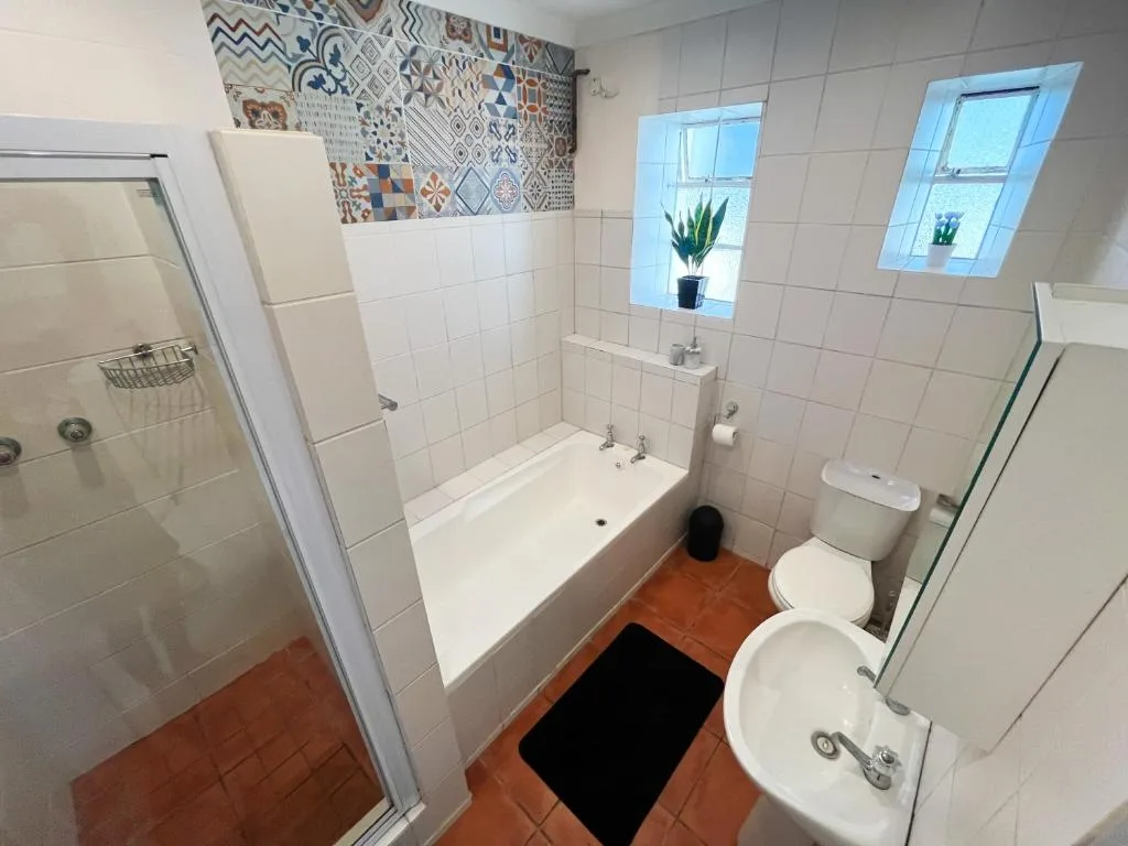 Bright bathroom with white tiles, bathtub, toilet, and patterned accent wall
