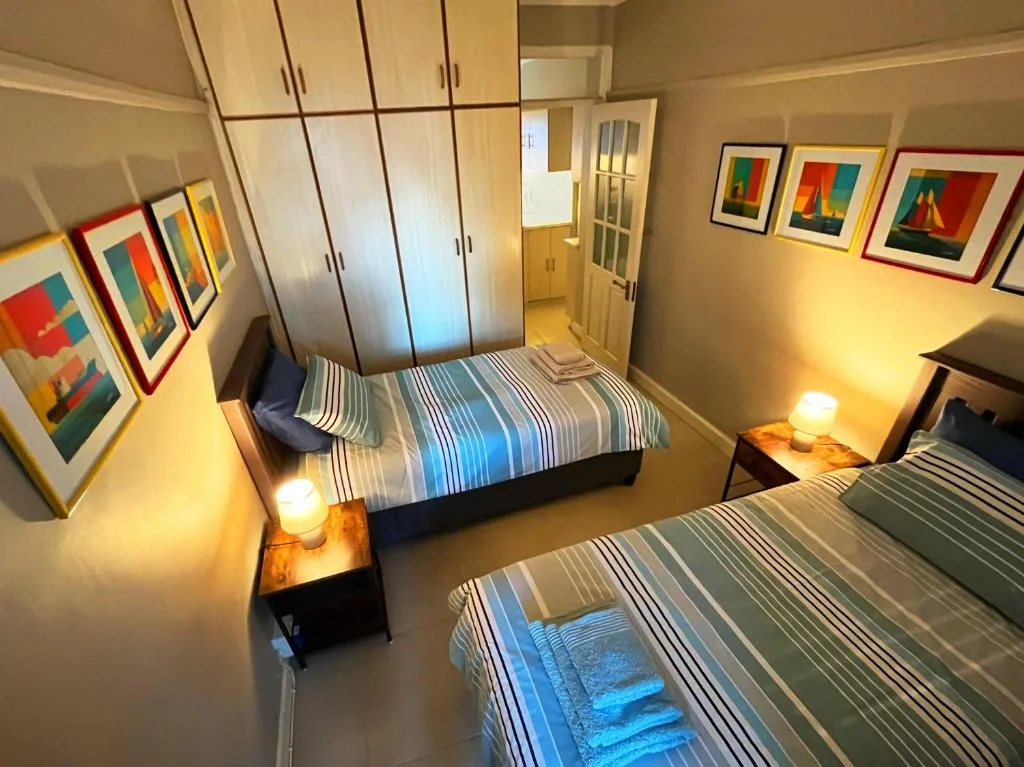 Bright bedroom with two beds, striped bedding, wooden wardrobes, and framed artwork